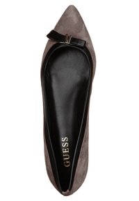 Mocassin plat en daim gris à bout pointu avec semelle intérieure en cuir noir, petit nœud noir orné d'un accent métallique, et marque "GUESS" à l'intérieur.