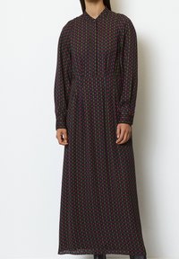 Robe longue et sombre avec un motif géométrique rouge et vert. Dotée d'un col et de manches longues, confectionnée dans un tissu léger.