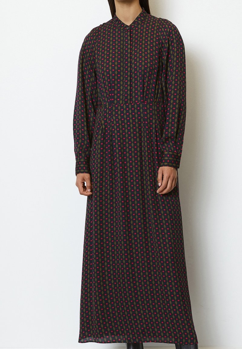 Robe longue et sombre avec un motif géométrique rouge et vert. Dotée d'un col et de manches longues, confectionnée dans un tissu léger.