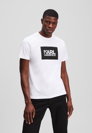 T-shirt en coton blanc à manches courtes, présentant un graphisme rectangulaire noir avec le texte "KARL LAGERFELD" affiché en lettres bien visibles.