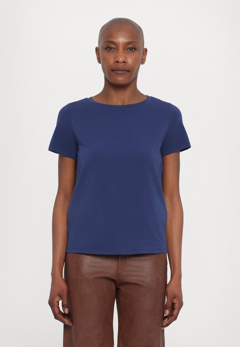 Σκούρο μπλε κοντομάνικο μπλουζάκι από μαλακό βαμβάκι, με στρογγυλή λαιμόκοψη και άνετη εφαρμογή, σε συνδυασμό με καφέ δερμάτινο παντελόνι.