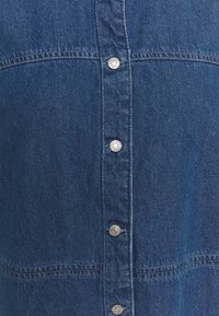 Mörkblå denimklänning med framknäppning, silverknappar och sydda detaljer. Har en strukturerad design och slät textur.