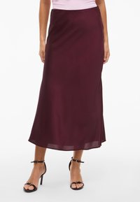 Burgundy satin midi-hame, jossa on sileä tekstuuri, sivuhalkio ja hulmuava muotoilu. Yhdistetty mustien nauhakaiutavien korkokenkien kanssa.