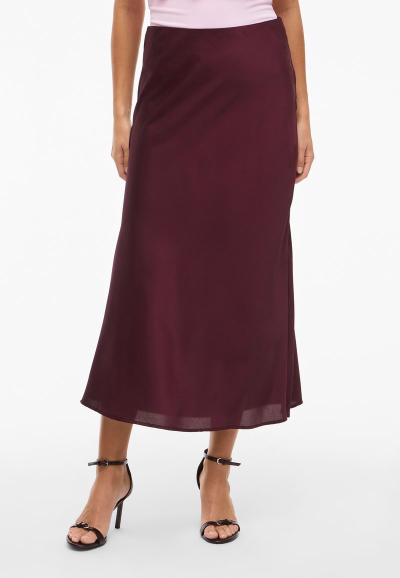 Burgundy satin midi-hame, jossa on sileä tekstuuri, sivuhalkio ja hulmuava muotoilu. Yhdistetty mustien nauhakaiutavien korkokenkien kanssa.