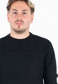 Czarny sweter z dzianiny o teksturowanym, geometrycznym wzorze, z okrągłym dekoltem i długimi rękawami.