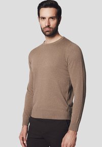 Brązowy sweter dzianinowy z długimi rękawami i okrągłym dekoltem, z prążkowanymi mankietami i dołem, które dodają tekstury. Idealny do noszenia na co dzień.