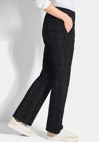 Pantaloni neri a fantasia con gamba dritta, caratterizzati da righe bianche e tasche laterali, abbinati a sneakers di colore chiaro.