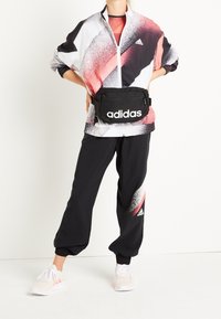 Sport jacket with red and black abstract pattern, paired with black tapered pants, a black fanny pack, and light-colored sneakers.