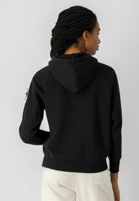 Sudadera negra con cordón, con detalles en blanco y puños acanalados. El material parece suave y cómodo. La vista trasera no muestra logotipos.