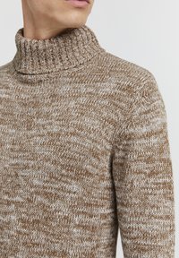 Brun og kremfarget melert strikkegenser med høy funnel-neck, som viser et strukturert stoff og en tettsittende design.