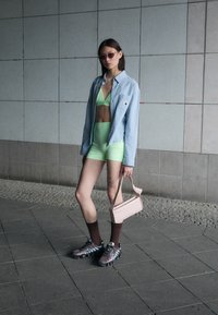 Light blue button-up shirt, bright green crop top and shorts, short brown socks, black and blue athletic shoes, and a pink handbag.