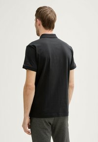 Sort polo-shirt lavet af bomuldsblanding, med klassisk krave og korte ærmer. Simpelt design med en subtil tekstur.