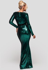 Smaragdgrøn palietkjole med lange ærmer og en tætsiddende silhuet. Har en sort taljedetalje og en skjult lynlås bagpå.