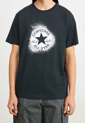 Czarny bawełniany t-shirt z okrągłym nadrukiem przedstawiającym gwiazdę oraz tekst "Converse" i "Chuck Taylor", otoczonym efektem rozprysku. Krótkie rękawy.