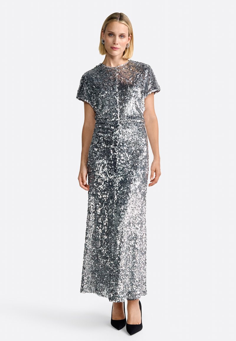 Silver sequin evening gown with a short-sleeve design, fitted silhouette, and floor-length cut. Paired with black high heels.