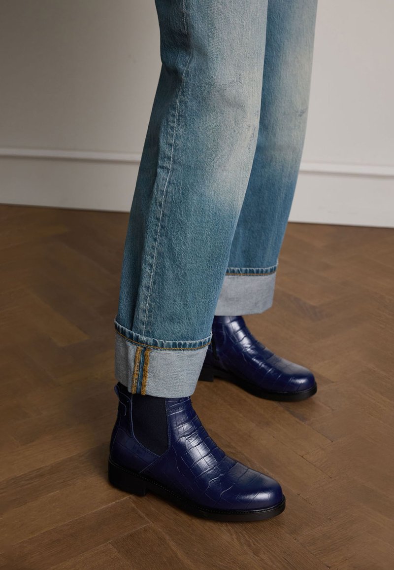 Blauwe croco-embossed leren enkellaarsjes met elastische zijpanelen, gecombineerd met lichtblauwe, opgerolde jeans met gele stiksels.