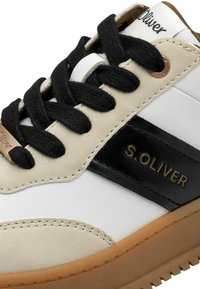 S. Oliver sneakers feature a beige and white leather upper with a glossy black stripe, black laces, and a gum rubber sole.