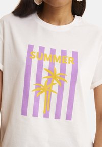 Camiseta de algodón blanca con rayas verticales moradas y un texto amarillo que dice "VERANO", con un gráfico de palmera como acento. Mangas cortas.