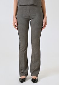 Pantaloni a righe nere e bianche svasati con una superficie liscia e dettagli laterali, abbinati a scarpe nere.
