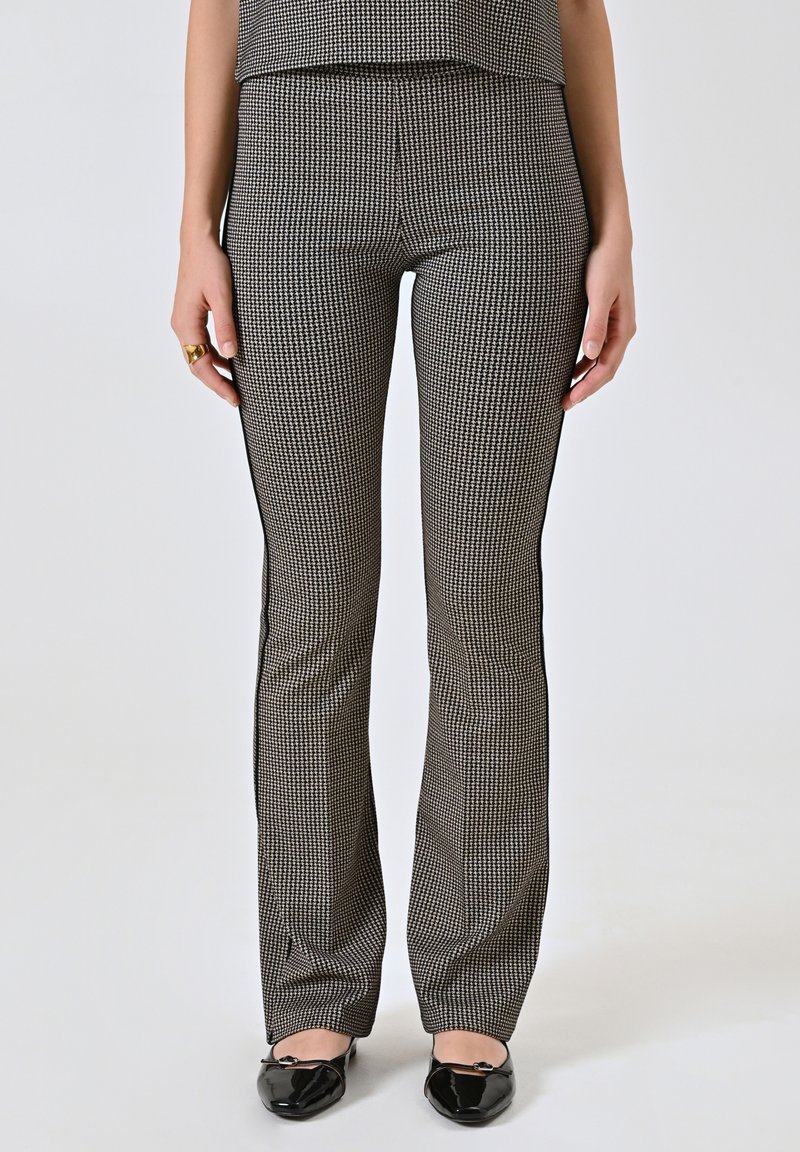 Pantaloni a righe nere e bianche svasati con una superficie liscia e dettagli laterali, abbinati a scarpe nere.