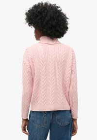Pull en maille torsadée rose avec un col haut, des poignets et un ourlet côtelés. Le dos présente des motifs texturés prononcés et une coupe décontractée.