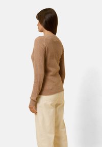 Beige geripptes Strickoberteil mit tailliertem Schnitt und langen Ärmeln, kombiniert mit hellen Cordhosen, von hinten betrachtet.