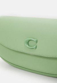 Sac à main en cuir vert clair avec un rabat incurvé et un logo en relief de la lettre C en vert à l'avant.