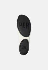 Suela de zapato en negro y crema con agarre texturizado. Presenta "PER" y tamaño "38" grabados en la superficie, con una forma aerodinámica y ergonómica.