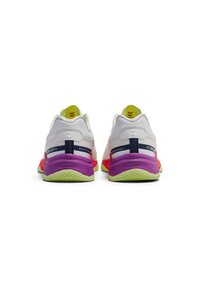 Chaussures de sport blanches avec des semelles intermédiaires violettes, des semelles intérieures jaune néon et des brides de talon noires estampillées "HB TOPFLIGHT" sur un fond blanc.