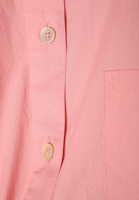 Tessuto della camicia rosa chiaro con una superficie liscia, caratterizzato da due bottoni e una tasca sul petto con dettagli di cucitura ordinati.