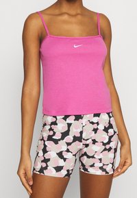 Rosa ärmlös linne med en vit Nike-logotyp, kombinerat med svarta shorts med ett flerfärgat abstrakt mönster i rosa och beige.