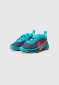 Kék és türkiz sportcipők, amelyek texturált szövet felsőrésszel, piros Nike pipa logóval és mintás tapadós gumitalppal rendelkeznek.