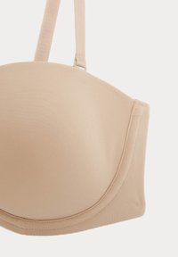 Beige vadderad bh med slät tyg, justerbara axelband och sömlös design. Diskret sömdetalj längs kanterna och bandet.
