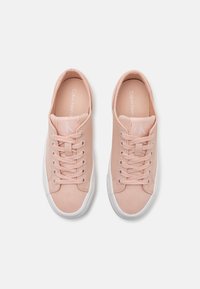 Pár světle růžových nízkých plátěných tenisek s bílými gumovými podrážkami a tkaničkami, s logem Calvin Klein na jazyku a stélkách.