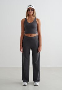 Szary sportowy stanik z dekoltem w kształcie litery V, zestawiony z szarymi spodniami z wysokim stanem. Dodatki to biała czapka i małe czarne okulary przeciwsłoneczne.