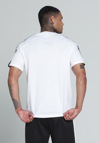 Camiseta blanca de manga corta con escote redondo y acentos negros en los hombros, hecha de una tela suave, combinada con pantalones negros.