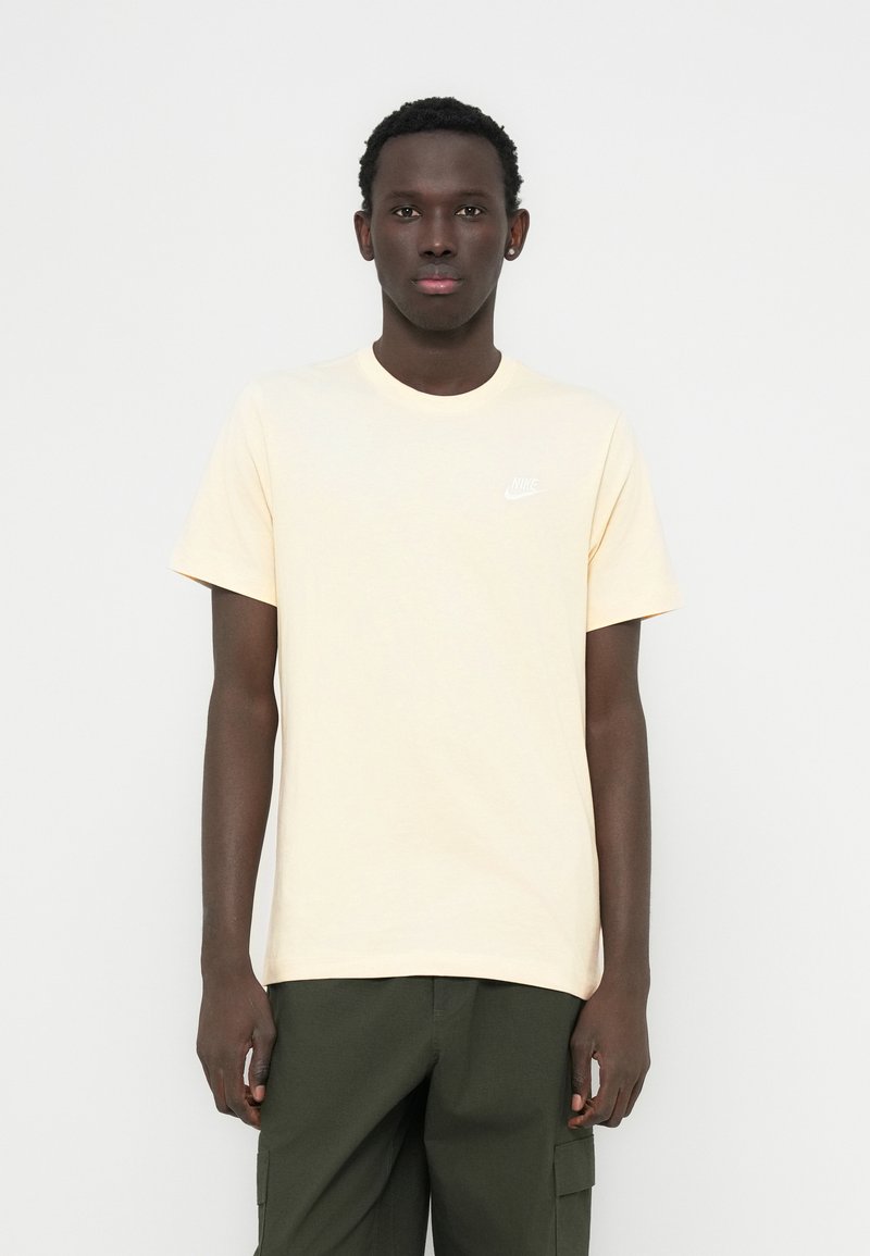 Ανοιχτόκίτρινη βαμβακερή κοντομάνικη μπλούζα με μικρό λευκό λογότυπο της Nike στο αριστερό στήθος, σε συνδυασμό με σκούρα πράσινο παντελόνι cargo.
