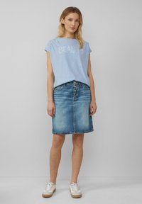 Lichtblauw T-shirt met korte mouwen met de tekst "BEAUTY", gecombineerd met een spijkerrok tot de knie. Model draagt witte sneakers met beige accenten.