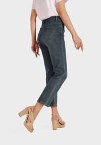 Jeans de mezclilla oscuros, de tiro alto y piernas rectas, con un diseño de cinco bolsillos y detalles de costura sutiles, combinados con tacones de plataforma color marrón claro.