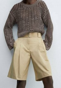 Pull en tricot marron avec une texture en maille ajourée, associé à un short plissé beige clair avec poches latérales et taille haute.