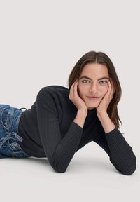 Schwarzer gerippter Rollkragenpullover mit langen Ärmeln, kombiniert mit blauen Jeans. Der Stoff ist strukturiert und sorgt für eine enganliegende Silhouette.