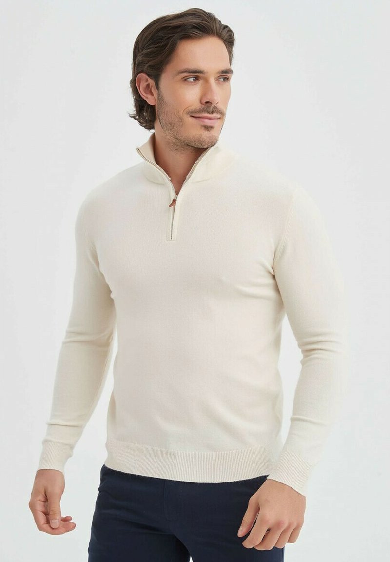 Pull-over crème avec col zippé, poignets et ourlet côtelés, fabriqué à partir d'un matériau doux, présentant une coupe ajustée.