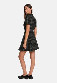 Robe à carreaux noirs avec des manches courtes, un corsage ajusté, une jupe évasée et un motif en damier blanc. Portée avec des mocassins noirs brillants.