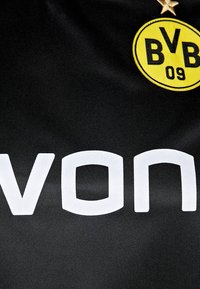 Mustapohjainen urheilupaita, jossa on suuri valkoinen "evon"-teksti, ympyränmuotoinen keltainen logo, jossa lukee "BVB 09", sekä kultatähtitieto logon yläpuolella.