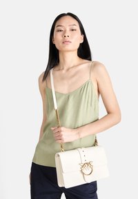 Μπεζ τσάντα με χρυσές λεπτομέρειες και λουλουδάτο μοτίβο. Λείο υλικό, δομημένο σχήμα και αποσπώμενη αλυσίδα ώμου.