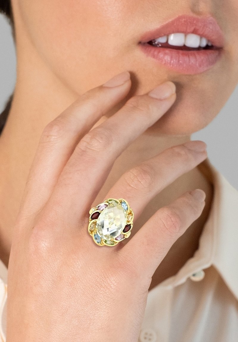 Bague en ton or avec une grande pierre ovale facettée de couleur jaune clair, entourée de plus petites pierres précieuses colorées (rouge, bleu, vert, rose).