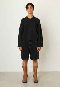 Black knitted sweater with a V-neck, paired with black denim shorts. Brown mid-calf boots with buckles complete the outfit.