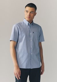 Kortærmet skjorte med blå og hvide lodrette striber, som har krave og brystlomme. Fremstillet af letvægtsstof.