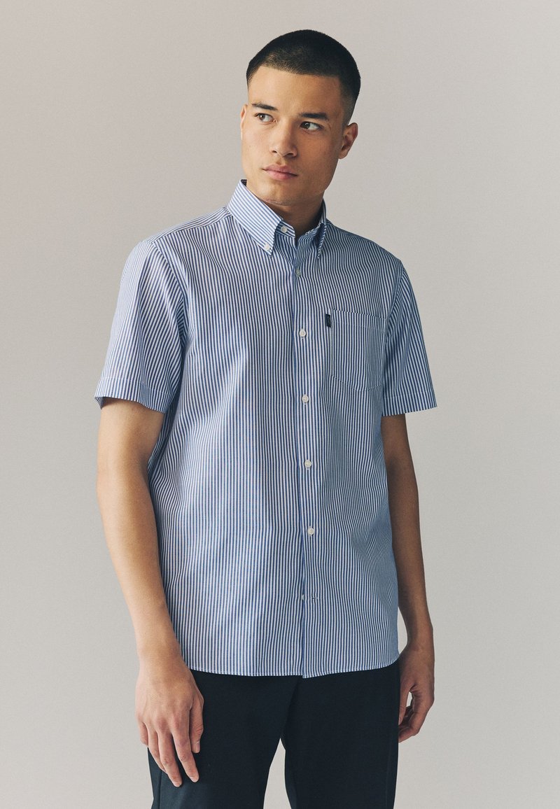 Kortærmet skjorte med blå og hvide lodrette striber, som har krave og brystlomme. Fremstillet af letvægtsstof.