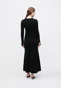 Czarna sukienka z długim rękawem, z dopasowanym gorsetem i rozkloszowanym dołem. Wykonana z miękkiego materiału, z okrągłym dekoltem i bocznymi rozcięciami.